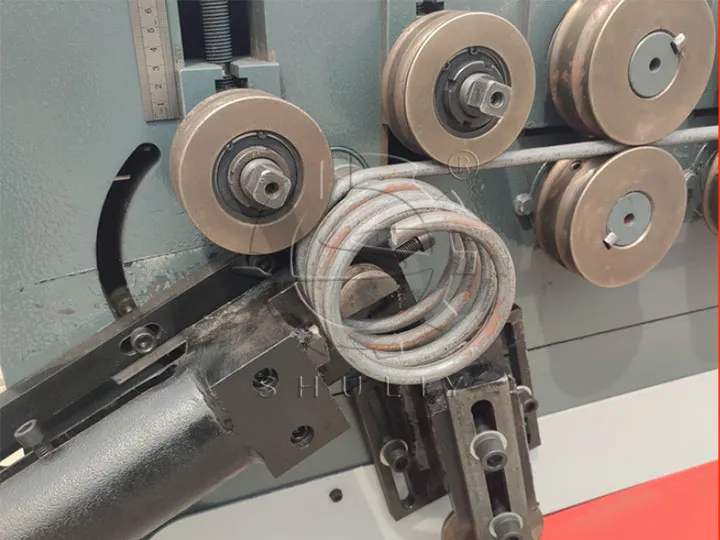 Close-up of rollers forming steel rebar into a circular coil